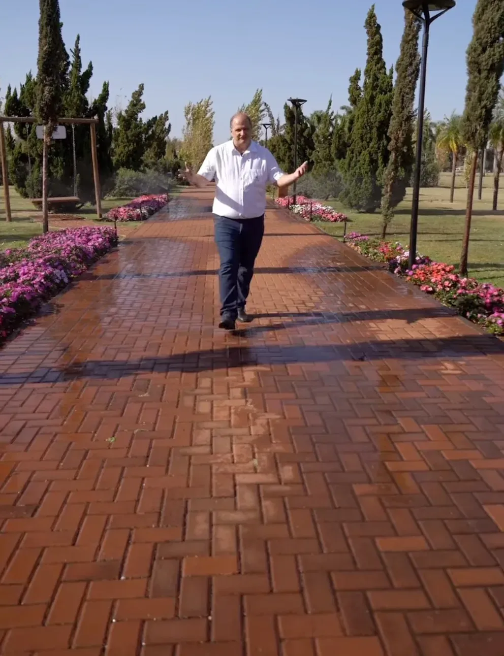 Caminho em jardim com canteiros floridos e irrigação no gramado
