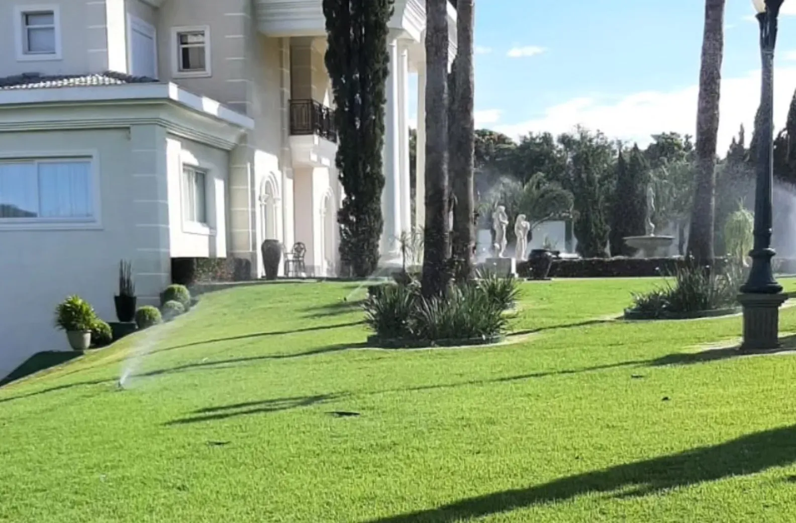 Gramado residencial amplo recebendo irrigação próxima à casa