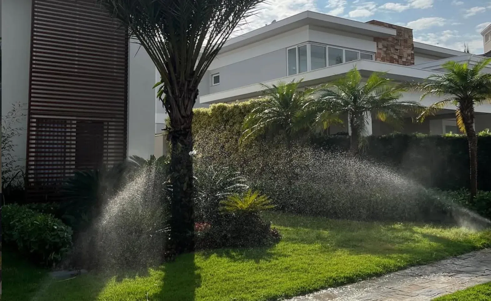 Jardim residencial com aspersores funcionando em frente a uma casa